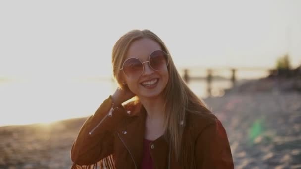 Joven hermosa chica en gafas de sol en la puesta del sol sonriendo en la cámara — Vídeos de Stock