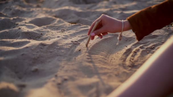 Bellezza ragazza disegna un cuore sulla sabbia sul tramonto spiaggia — Video Stock