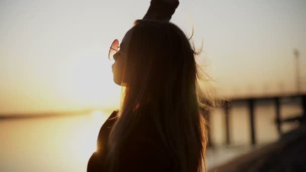 Jovem menina bonita em óculos de sol no pôr do sol sorrindo na câmera — Vídeo de Stock