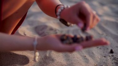 Genç kız hangi toplanan On Beach, gün batımı arka plan içinde kabuklar kadar tutun