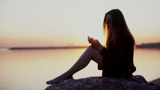 Mulher Smartphone em vestido vermelho SMS SMS usando o aplicativo no telefone inteligente no pôr do sol da praia . — Vídeo de Stock