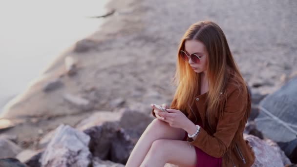 Smartphone vrouw in rode jurk sms-berichten met behulp van app op smartphone bij strand zonsondergang. — Stockvideo