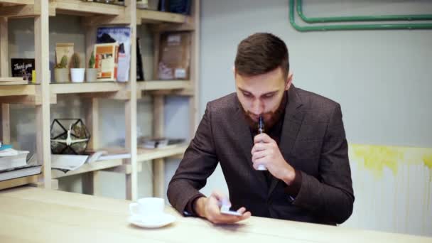 Vousatý muž v obleku je kouření e cigarety vape, u smartphonu — Stock video