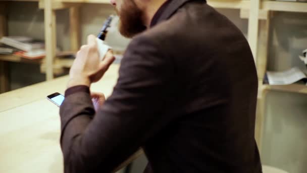 Γενειοφόρος άνδρας με κοστούμι είναι το κάπνισμα vape e-τσιγάρο, κουβεντιάζοντας με έξυπνο τηλέφωνο — Αρχείο Βίντεο