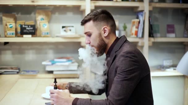 Vousatý muž v obleku je kouření e cigarety vape, chattingphone a pití kávy — Stock video