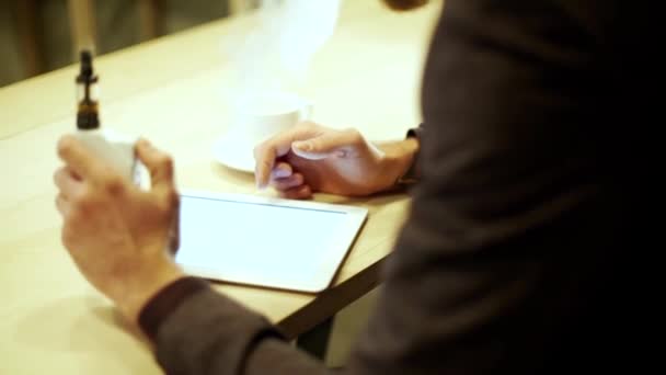 Primer plano hombre de negocios en un traje de lectura en la tableta con un vapor de cigarrillo electrónico — Vídeos de Stock