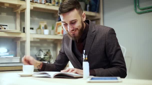 Beadrded man is reading magazine with e-cigarette vape in cafe — Stock Video