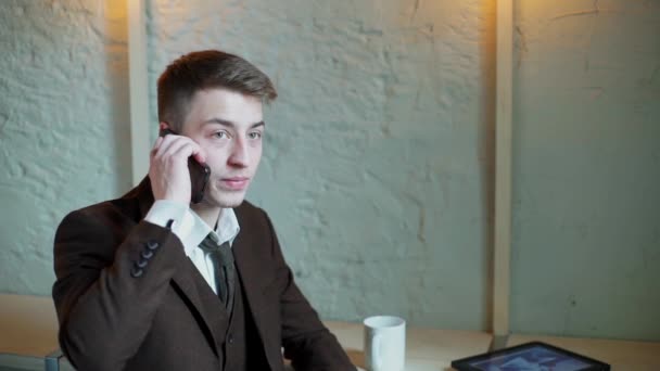 Серйозний бізнесмен працює на планшетному комп'ютері в кафе і розмовляє телефоном — стокове відео