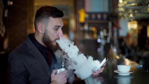 Modern hipster businessman drinking coffee in cafeand working on tablet smoking e-cigarette vape — Stock Video
