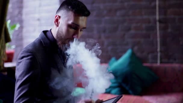 Moderna hipster affärsman dricka kaffe i cafeand arbetar på tablet rökning e-cigarett vape — Stockvideo