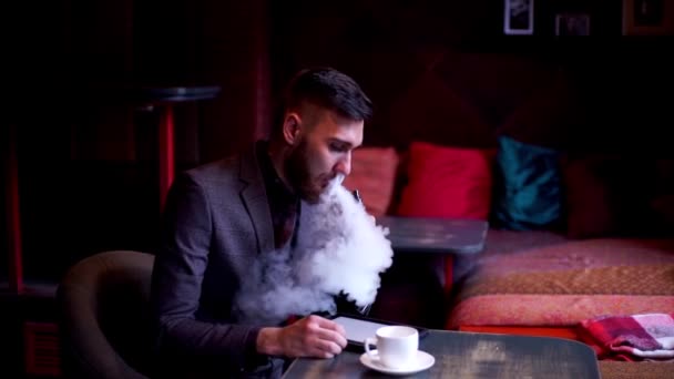 Modern hipster businessman drinking coffee in cafeand working on tablet smoking e-cigarette vape — Stock Video