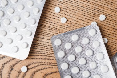 top view on aluminum packaging of pills on a wooden table. White round pills for diseases in packages and scattered on the table. Copy space