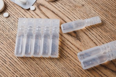 ampoules with liquid medicine and white round pills on wooden background