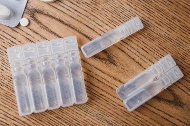 ampoules with liquid medicine and white round pills on wooden background