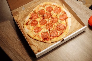 pepperoni pizza in a delivery box on a wooden table with bell pepper in the foreground