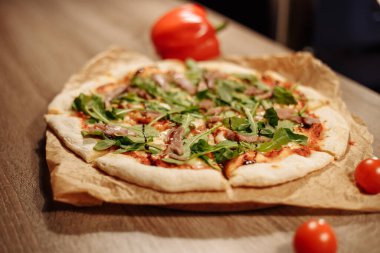 Bitkilerle dolu taze pizza, ton balığı ve balzamik sos, ahşap bir masada, rahat bir kafede, arka planda dolmalık biber.