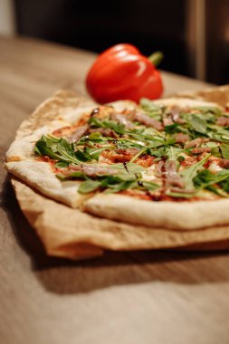 Bitkilerle dolu taze pizza, ton balığı ve balzamik sos, ahşap bir masada, rahat bir kafede, arka planda dolmalık biber.