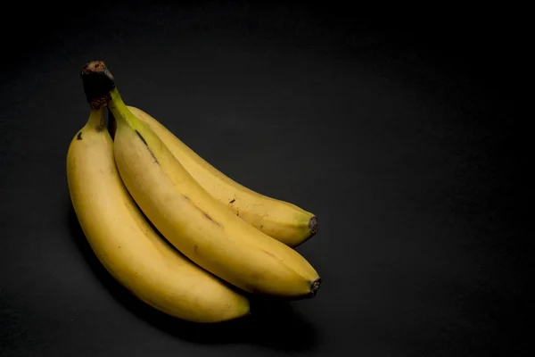 Tre bananer på en mörk bakgrund Stockbild