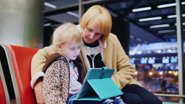 Madre e hija esperando su vuelo, niña jugando en una tableta — Vídeo de stock