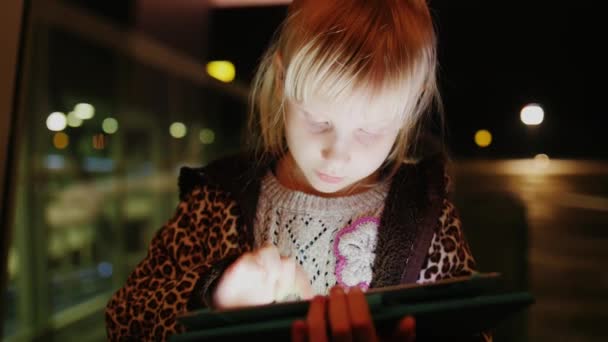 Uma menina desfruta do tablet no fundo de uma grande janela com reflexos — Vídeo de Stock