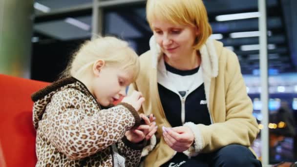 Madre e hija sentadas en el aeropuerto, y jugando por teléfono — Vídeos de Stock