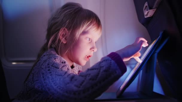 Маленька дівчинка летить на літаку і грає на планшеті — стокове відео
