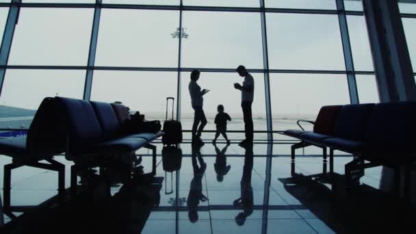 Люди с устройствами на фоне большого окна в аэропорту — стоковое видео