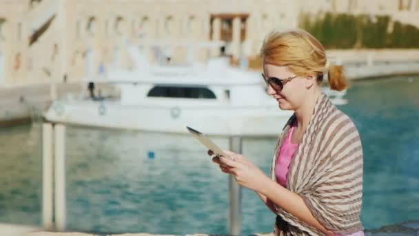 Женщина-туристка наслаждается планшетом на фоне яхт — стоковое видео