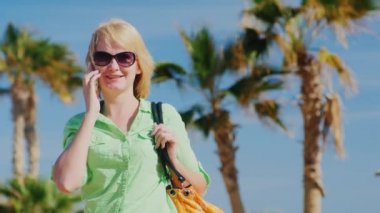 Mutlu turist telefonla bir arka plan mavi gökyüzü ve palmiye ağaçları üzerinde konuşuyor.