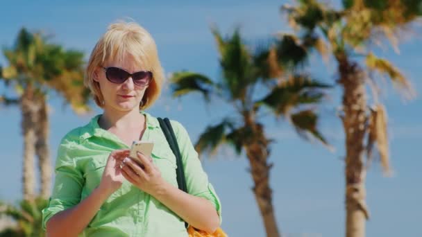 Un turista con gafas y una bolsa sobre su hombro SMS — Vídeos de Stock