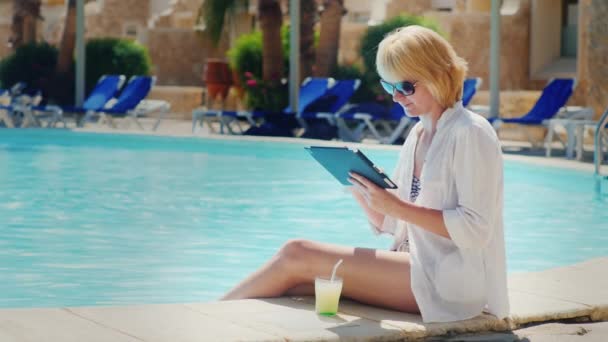 Woman relaxing by the pool, enjoy a tablet, drink a cocktail — Stock Video