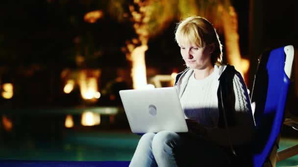 Uma jovem usa um laptop na beira da piscina — Vídeo de Stock