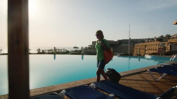 Steadicam shot of Woman with travel bag walking on recreation area along the pool — Stock Video