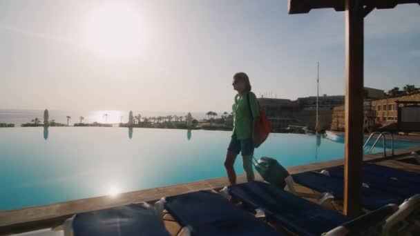 Steadicam heta: turist promenader längs poolen med solstolar. Lucky resväska på hjul — Stockvideo