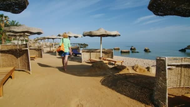 Steadicam shot: turista con una bolsa de playa caminando por la playa — Vídeo de stock