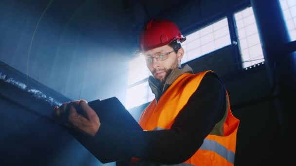 Der Bauarbeiter oder Ingenieur, der mit Dokumenten gegen das Fenster und die Sonnenstrahlen arbeitet — Stockvideo