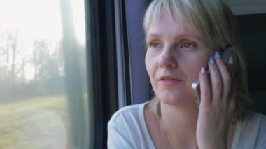 Bir trenin cam kenarında oturan, telefonda konuşurken bir sarışın kadın