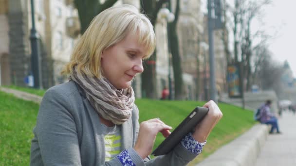 Szőke nő élvezi a tabletta a parkban — Stock videók