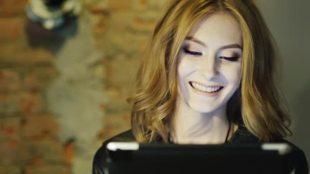 Una joven sonriendo, disfrutando de la tableta en la cafetería — Vídeos de Stock