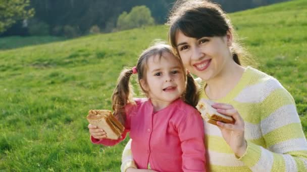 Moeder en dochter broodjes eten op een picknick — Stockvideo