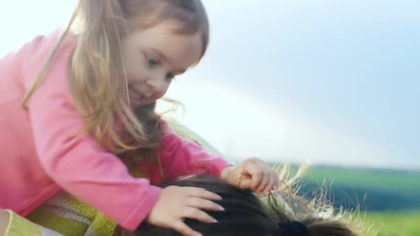 Moeder en dochter knuffelen en spelen op het gras — Stockvideo