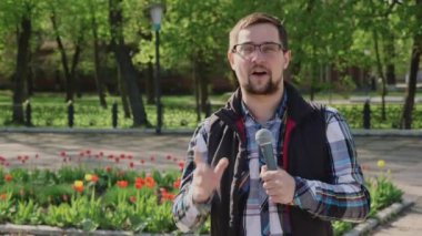 Bir mikrofon ile Male muhabir haber kamerası söyler. Ağaçlar ve çiçeklerle bir arka plan üzerinde bahar parkta olması gerektiği