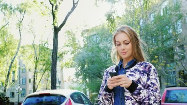 Femme attrayante marchant dans la ville, bénéficie d'un smartphone. Les rayons du soleil tombent beaux moments forts — Video