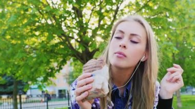Çekici kadın parkta, bir sandviç yeme müzik