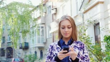 Kız şehrin içinden Smartphone'da yazarak gider. Güneş güzel aydınlatır