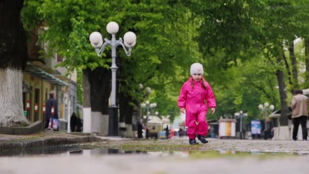 Dziewczyna w kombinezon i gumowe buty, uruchomiony przez kałuże — Wideo stockowe