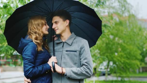 Mujer joven y un hombre elegante de pie en la calle bajo un paraguas. Está lloviendo — Vídeos de Stock