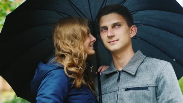 Junges schönes Paar, das unter einem Regenschirm steht. Es regnet — Stockvideo