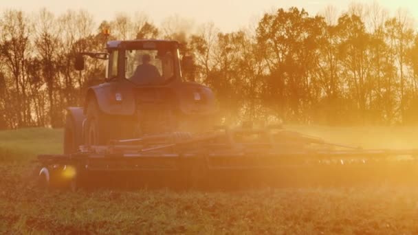 Трактор вспахивает поле на закате — стоковое видео