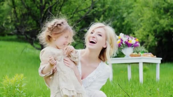 Mor och dotter 4-5 år spelar på gröna gräsmattan. I bakgrunden, ett bord med godis för en picknick — Stockvideo